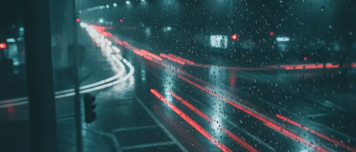 Rain on a traffic camera lens: water drops blur the image and wet asphalt reflects headlights